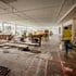 Bauarbeiter in Warnweste in einem großen, hellen Büro-Rohbau mit Baumaterialien, Leitern und Werkzeugen.