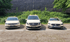 Drei helle Taxis, zwei Mercedes und ein VW, parken nebeneinander auf einem Pflastersteinplatz vor einer grünen Wand.