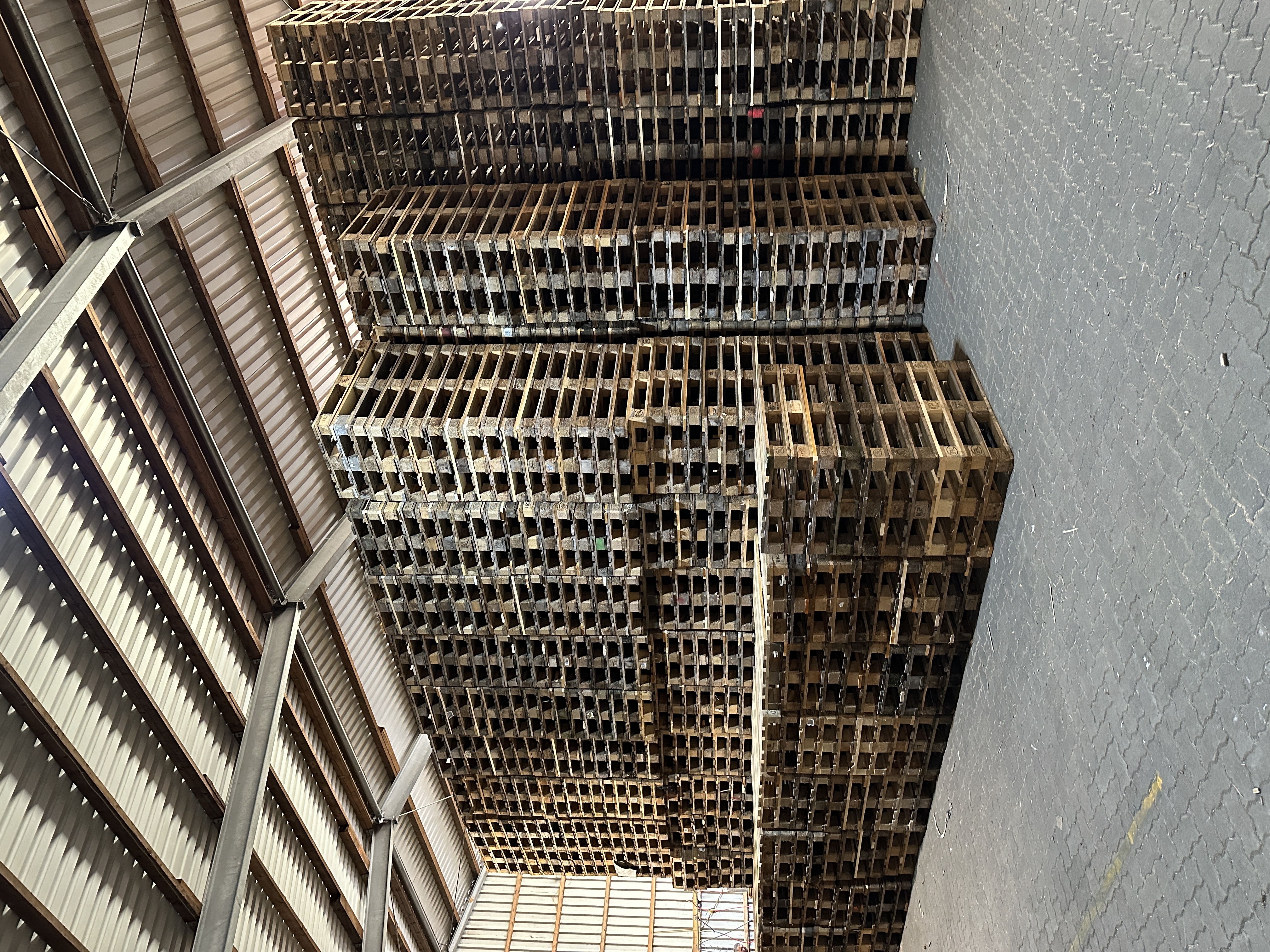 Hohe Stapel von Holzpaletten im Lagerhaus, mit Metallstreben und Wellblechwänden.