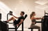 Mann und Frau trainieren an modernen, schwarzen Kraftgeräten in einem hellen Fitnessstudio mit minimalistischem Design.