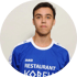 Porträt eines jungen Mannes mit kurzem dunklem Haar, der ein blau-weißes Sporttrikot mit dem Aufdruck „RESTAURANT KORELL“ trägt, vor neutralem Hintergrund.