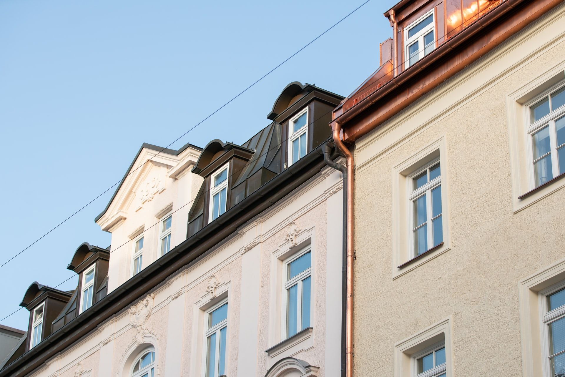 Fassade eines sanierten Mehrfamilienhauses mit Gauben vor blauem Himmel
