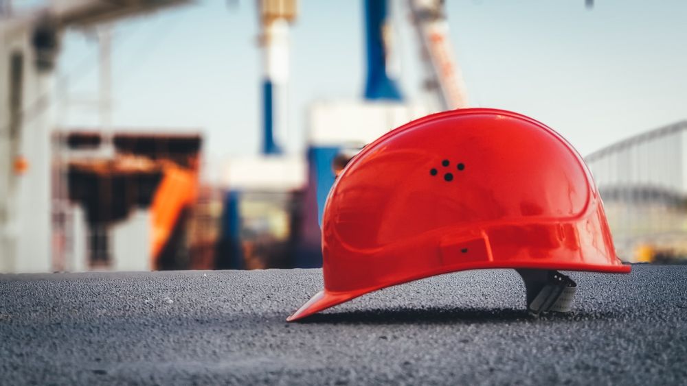 Roter Schutzhelm auf Asphalt vor einer Baustelle als Symbol für Projektsteuerung und Bauleitung
