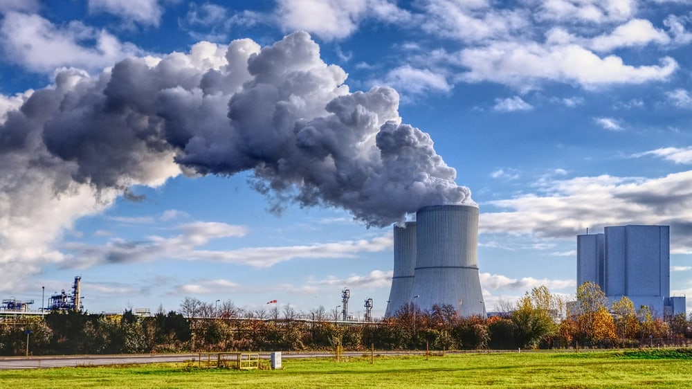 Kraftwerk mit dampfendem Kühlturm unter blauem Himmel