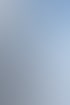 Ein Segler arbeitet hoch oben an einem weißen Segel unter blauem Himmel und strahlender Sonne.