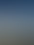 Flugzeugflügel über einer Landschaft mit Feldern und vereinzelten Wolken unter blauem Himmel.