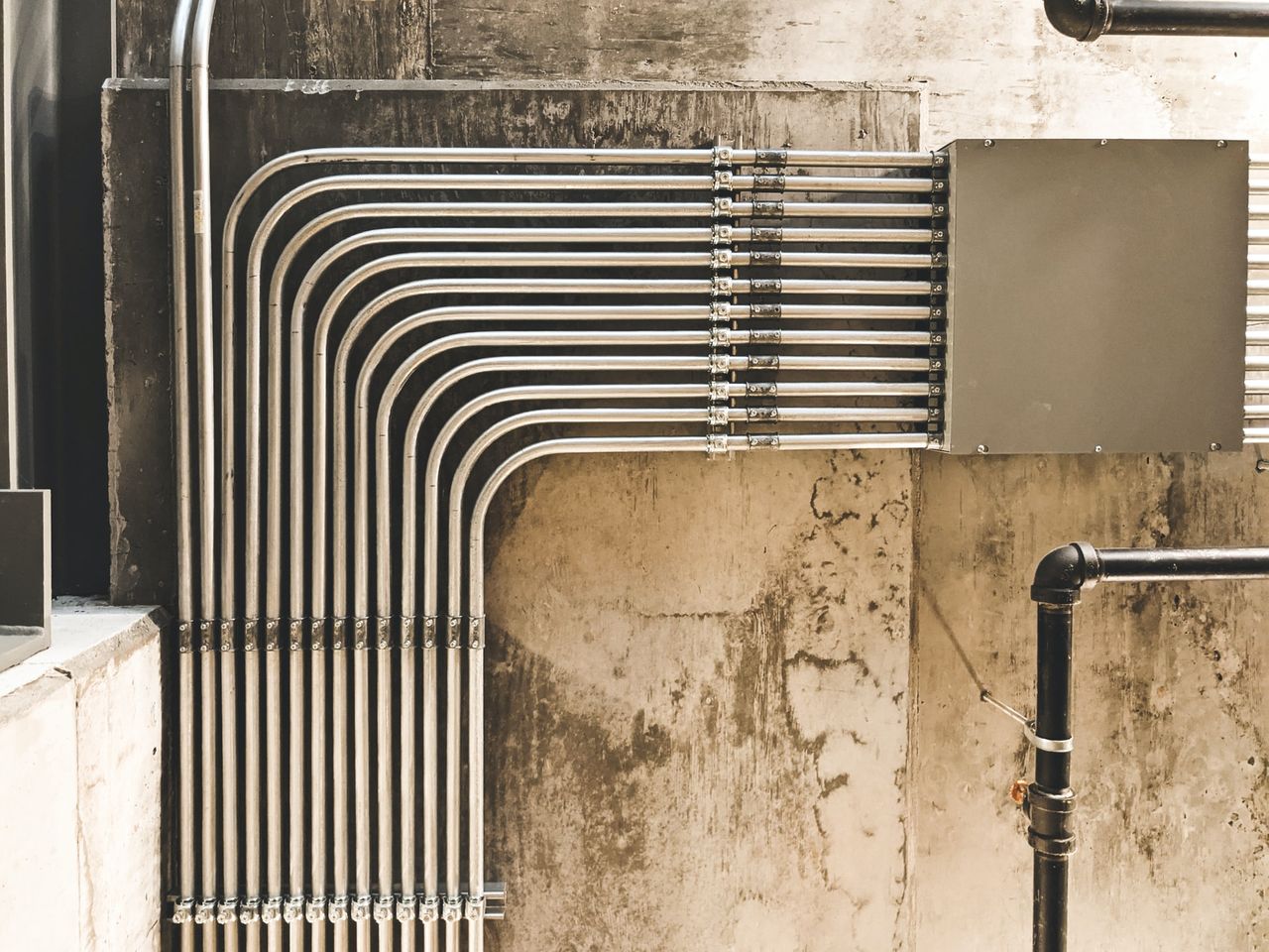 Parallel verlegte Metallrohre an einer Betonwand